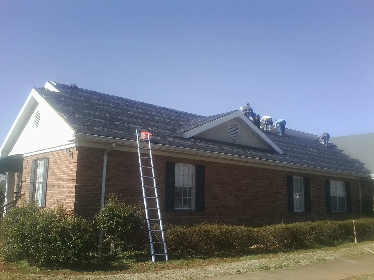 Crew tearing shingles off a brick ranch roof with a ladder set — Emergency Roof Repair work by our crew in Zanesfield