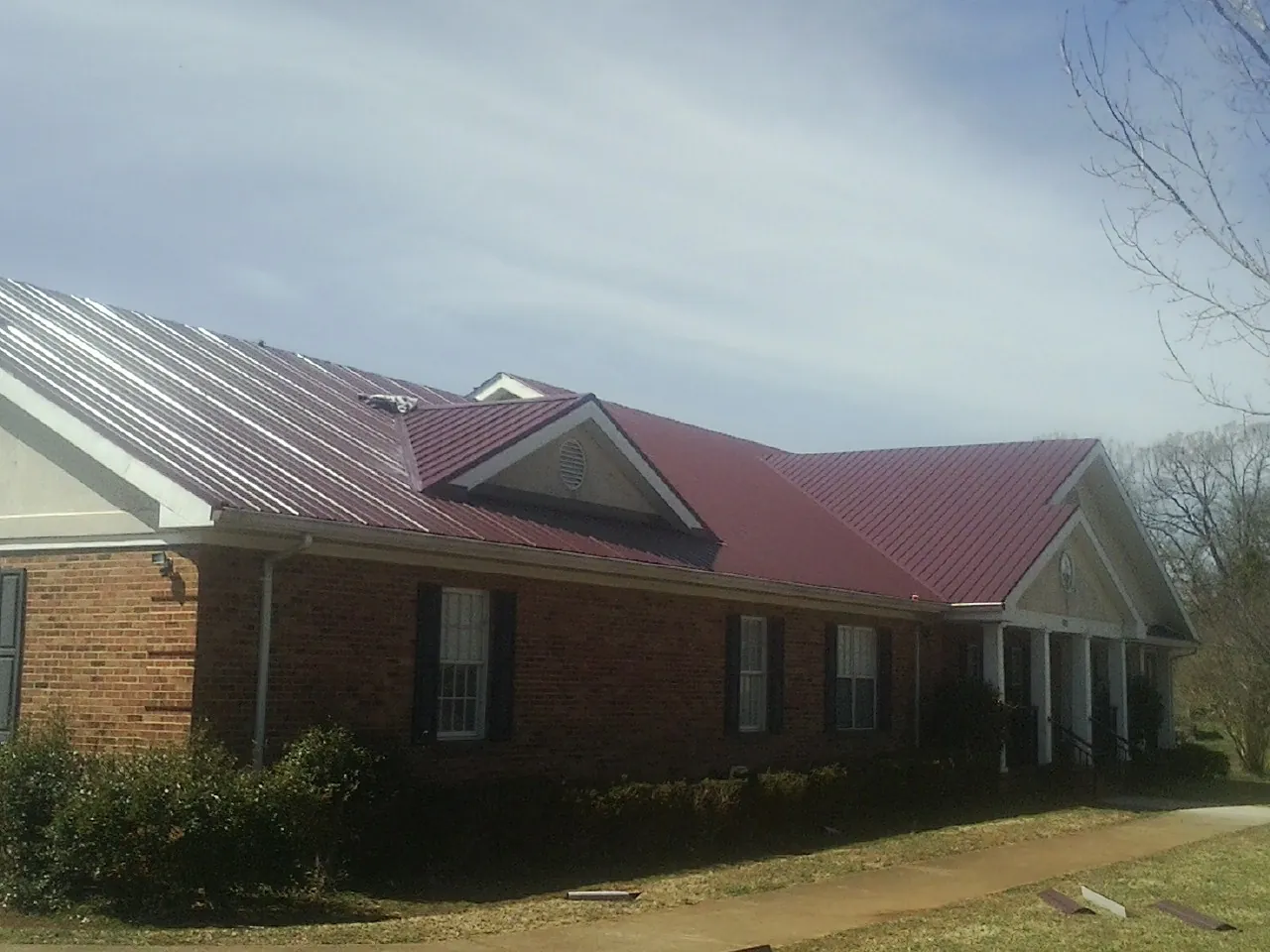 Red metal roof with gabled entries on a long brick building, from a Hail Damage Roof Repair job in Zanesfield
