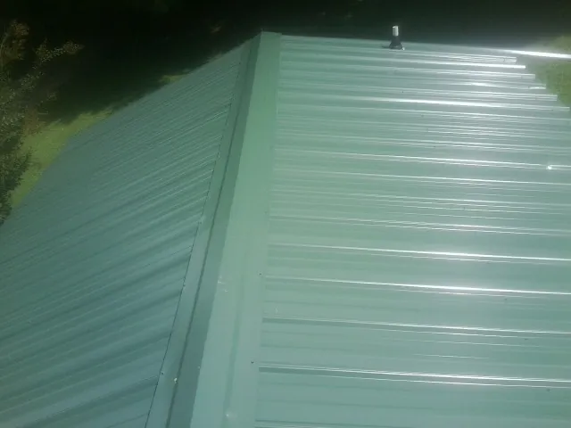 New green metal panels meeting at the ridge of a roof — Flat Roof Repair work by our crew in Zanesfield