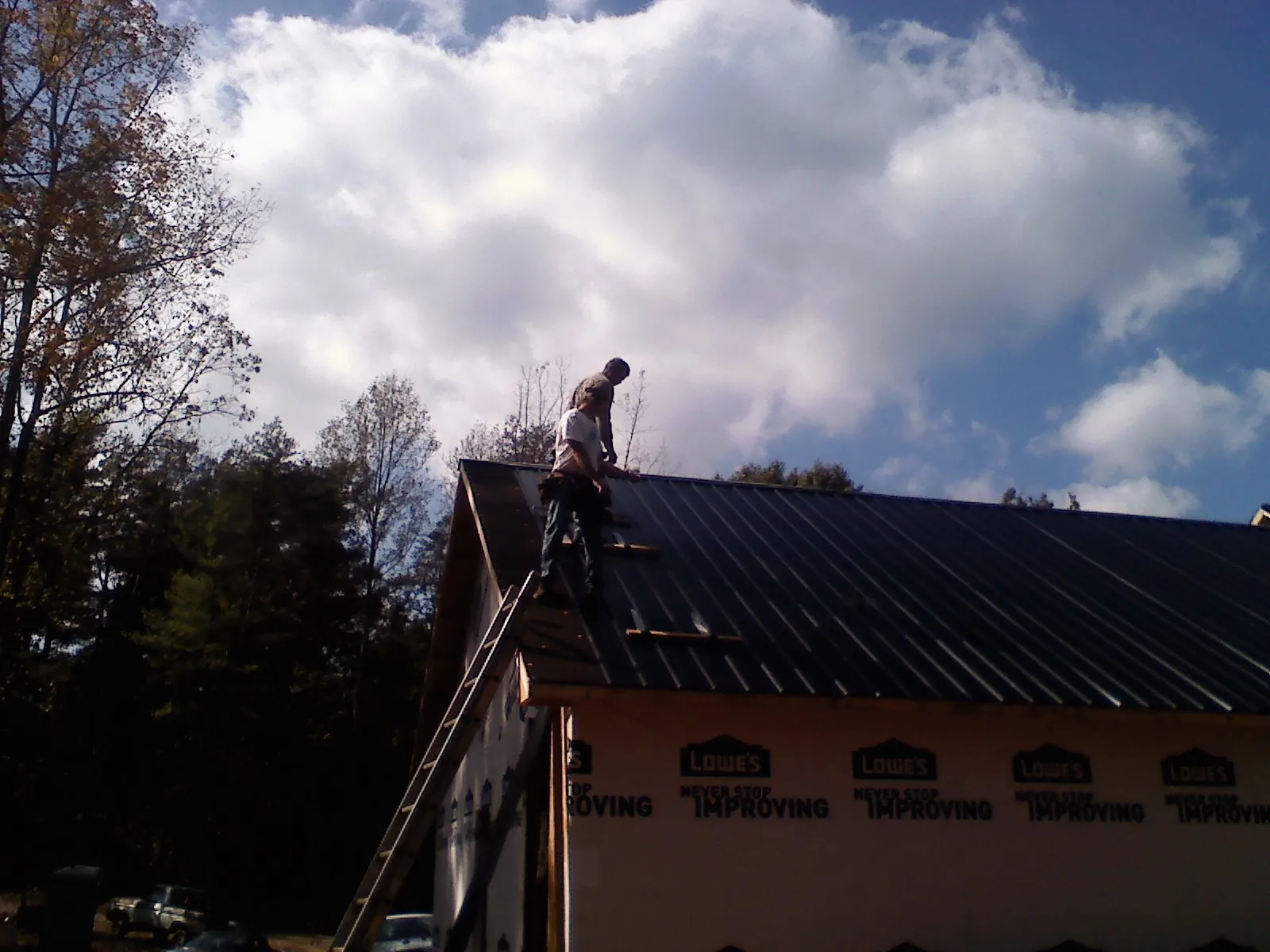 Roofer fastening dark metal panels high against a cloudy sky, from a Roof Inspection job in Zanesfield