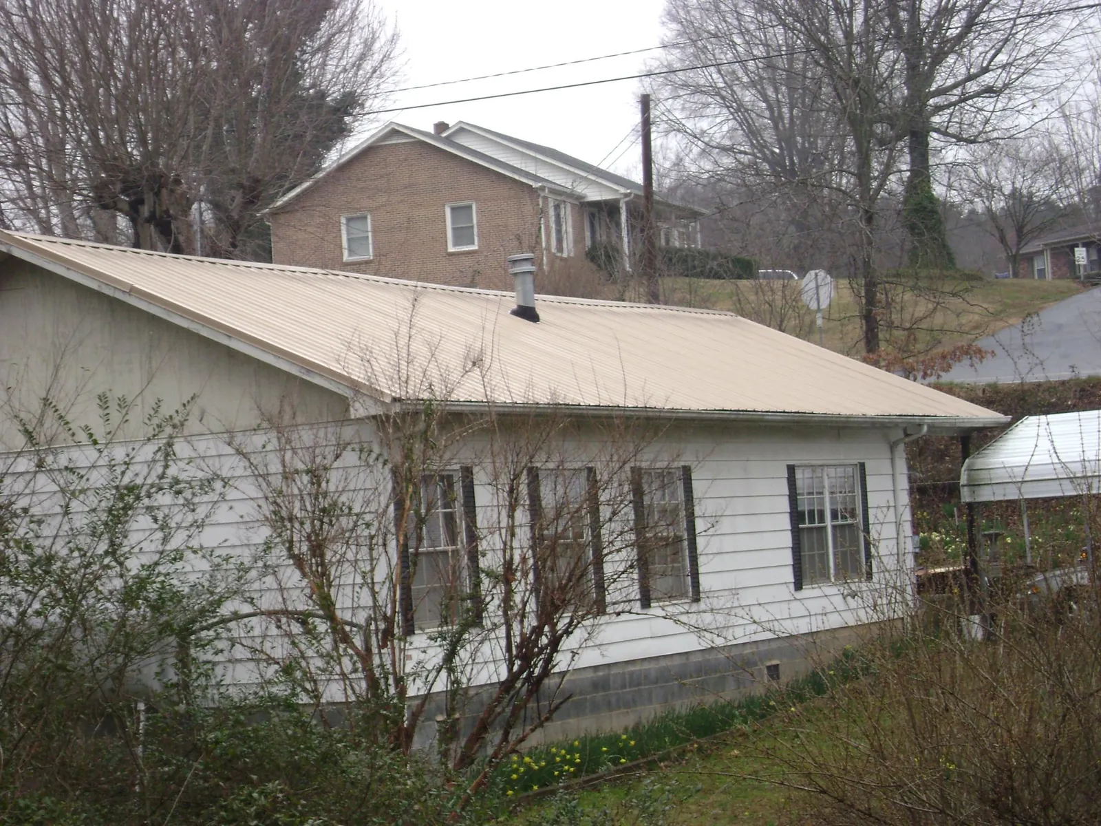 Tan metal roof on a white sided house set into a hillside — Commercial Roofing by Roofing Brothers in Zanesfield